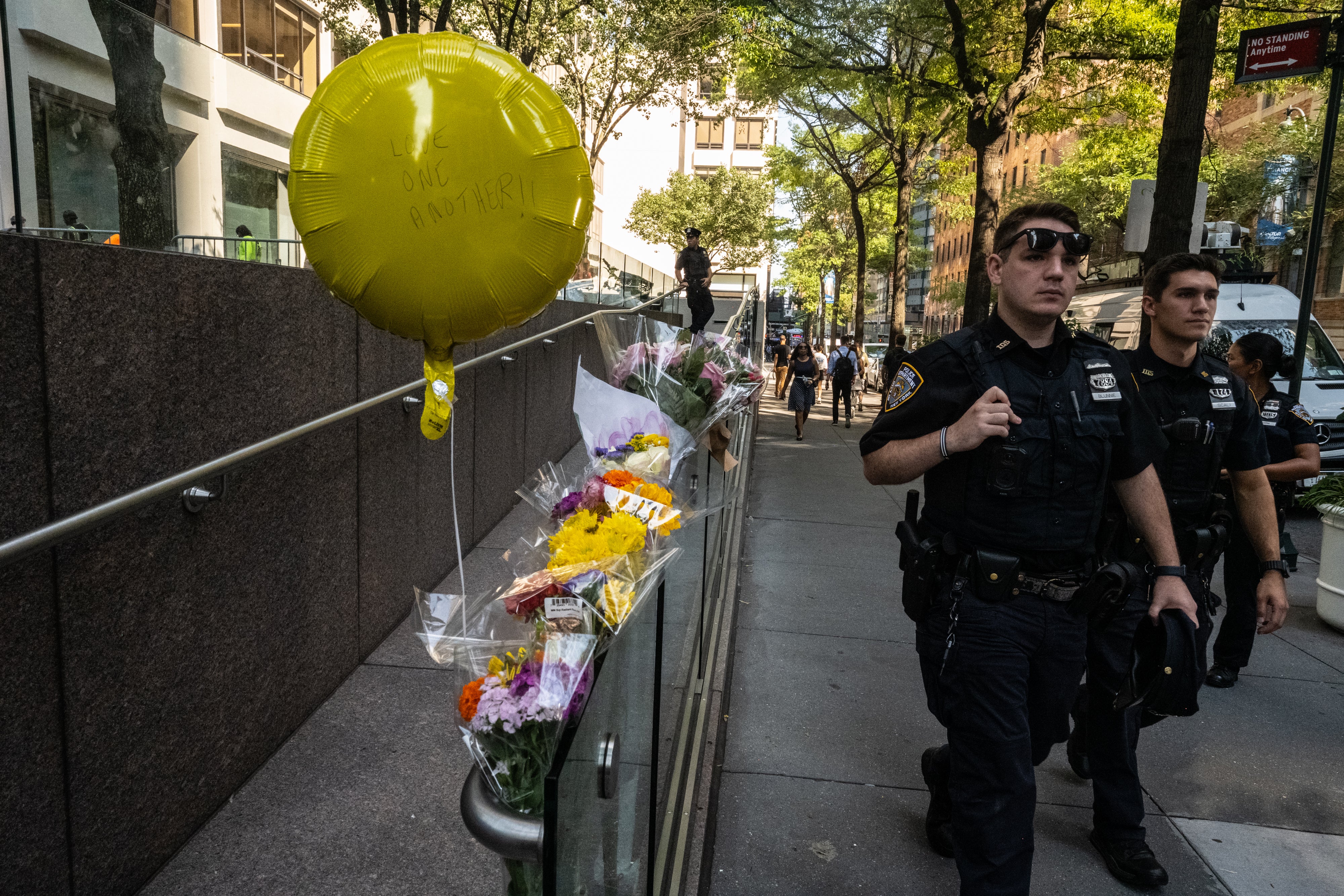 NYPD officers walk past flowers placed at 345 Park Avenue to honor those killed by Shane Tamura