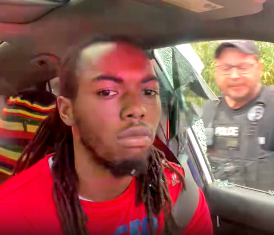 William McNeil looks at his cell phone camera as Officer D. Bowers breaks his car window