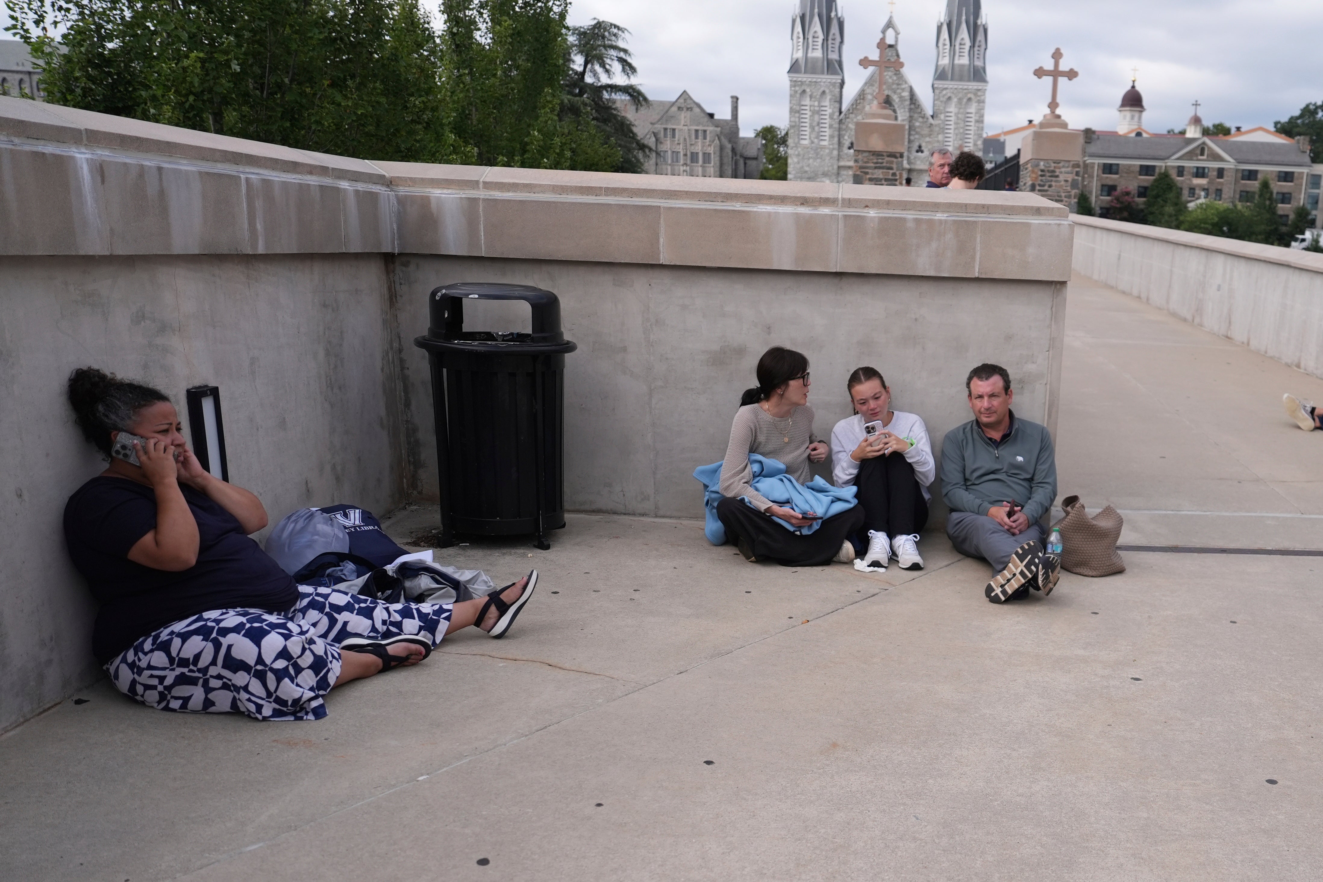 People shelter behind a wall at the Villanova University campus where an active shooter was reported Thursday, Aug. 21, 2025, in Villanova, Pa