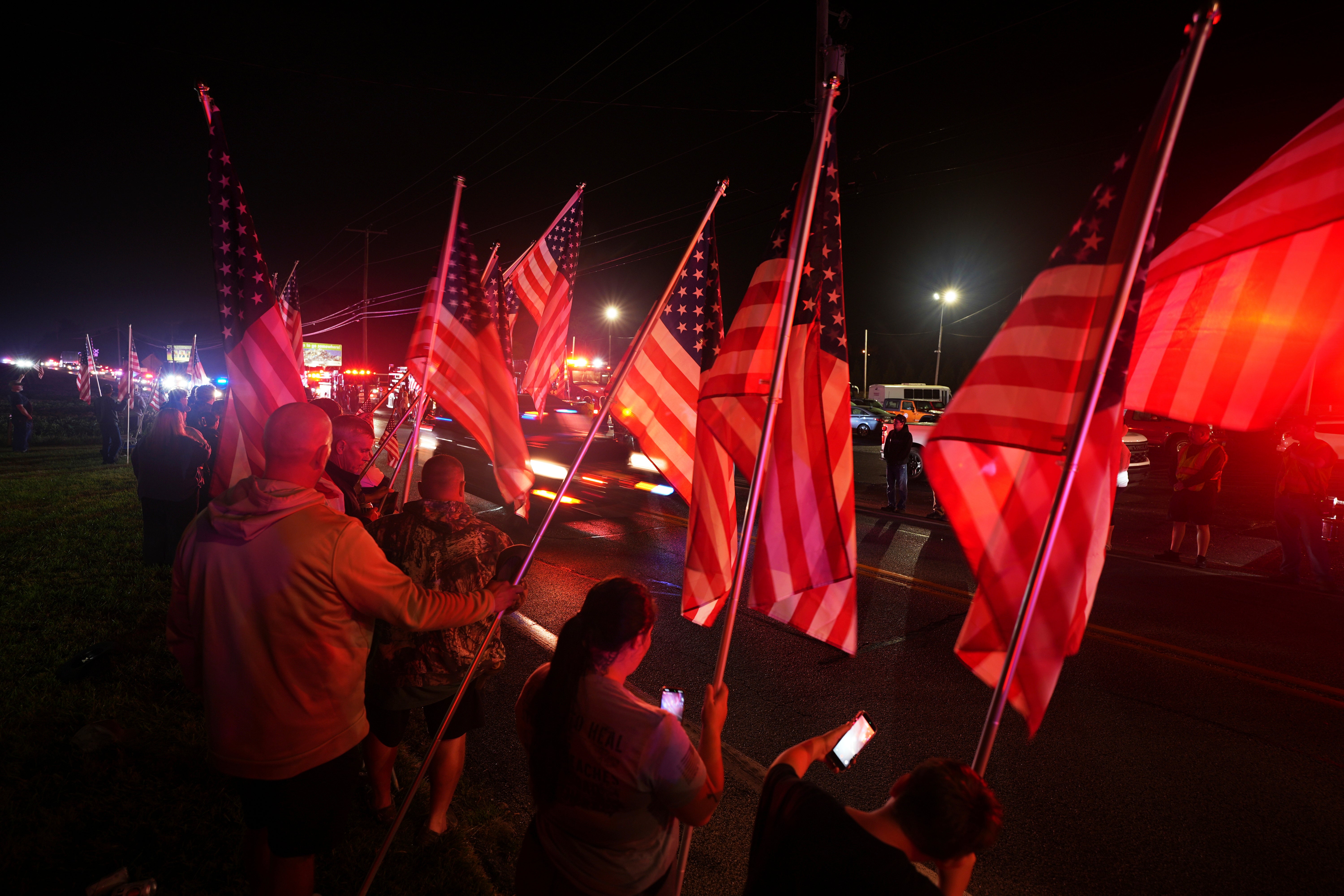 People held American flags to salute a procession of emergency vehicles to the coroner’s office after the fatal shooting of three Pennsylvania police officers.